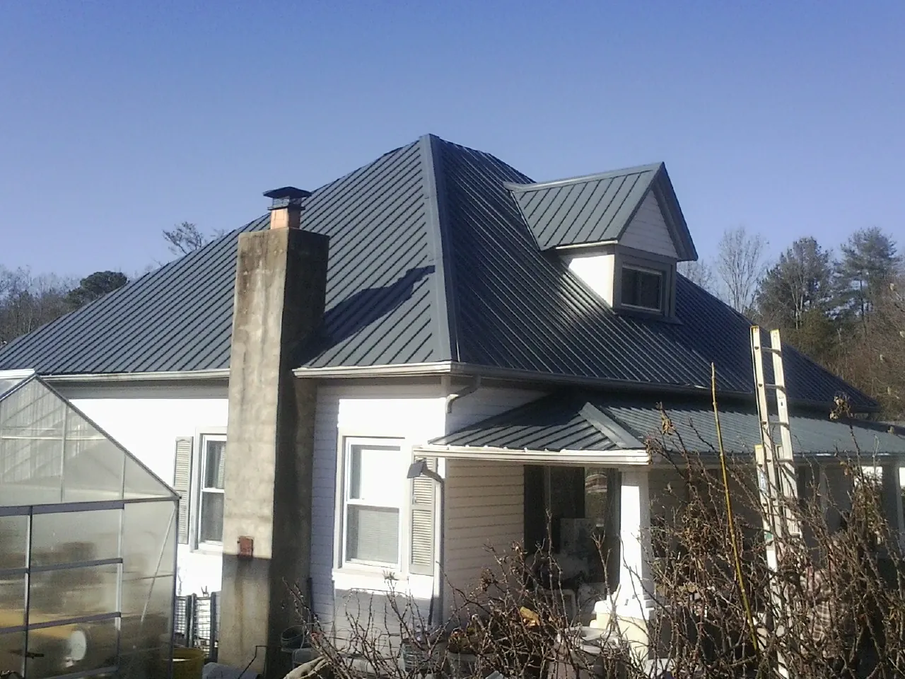 Dark blue standing seam metal roof on a white farmhouse with dormer — Slate & Tile Roof Repair by Roofing Brothers in Vancouver