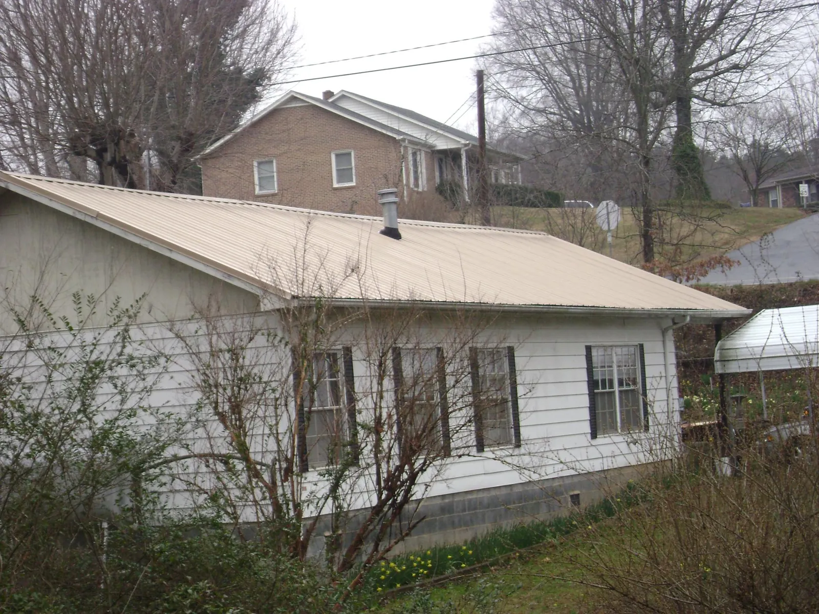 Tan metal roof on a white sided house set into a hillside — Commercial Roofing by Roofing Brothers in Vancouver